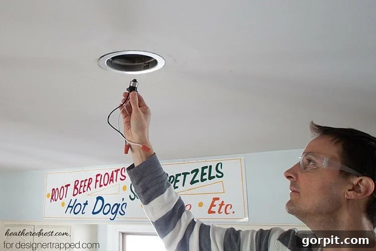 Screwing the conversion kit's lighting harness into the existing recessed light socket.