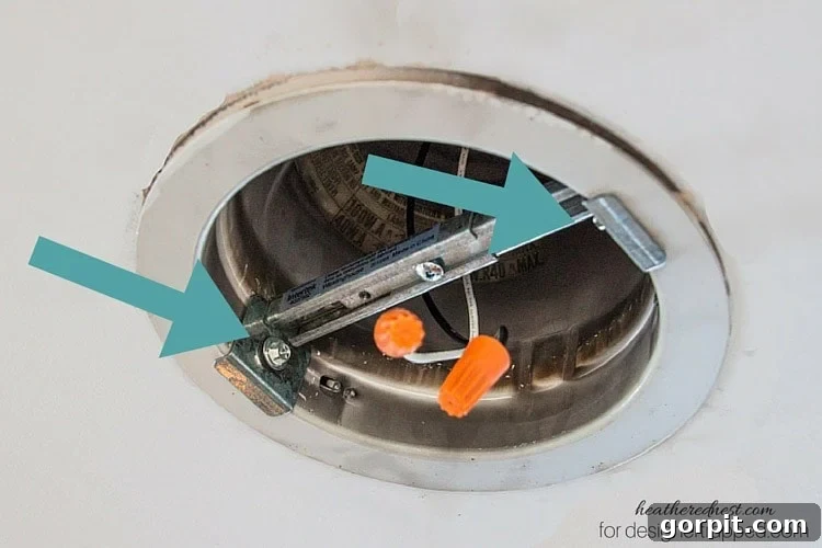 Attaching the cross brace to the recessed light housing with screws for a secure installation.