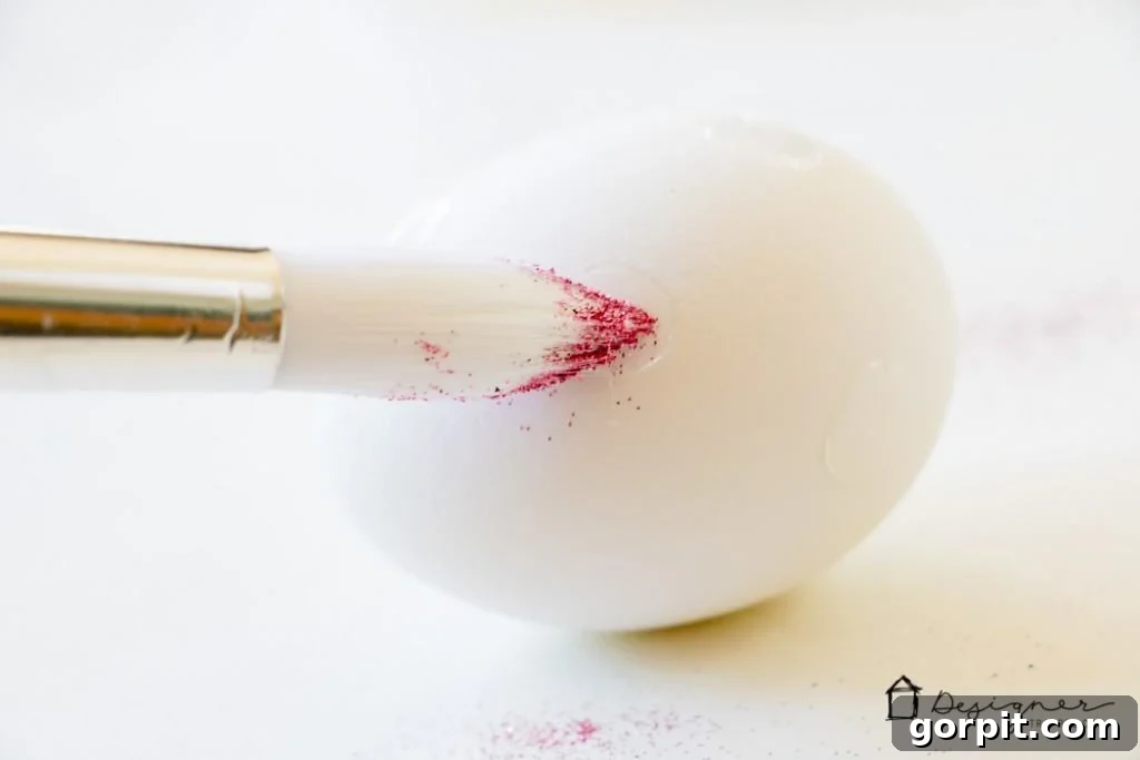 Applying glitter to an exposed glue dot on an Easter egg using a fine artist's brush.