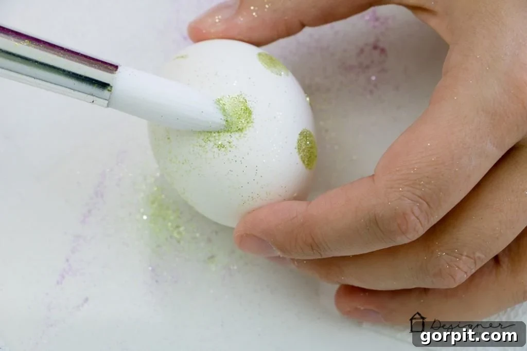 Close-up of glitter being applied to an Easter egg dot for a dazzling effect.