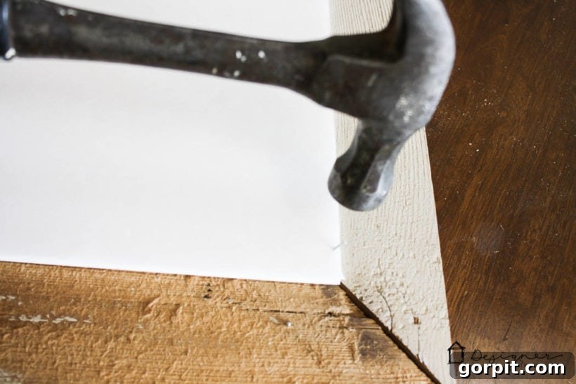 Securing mounted art to the back of a DIY picture frame with a staple gun.