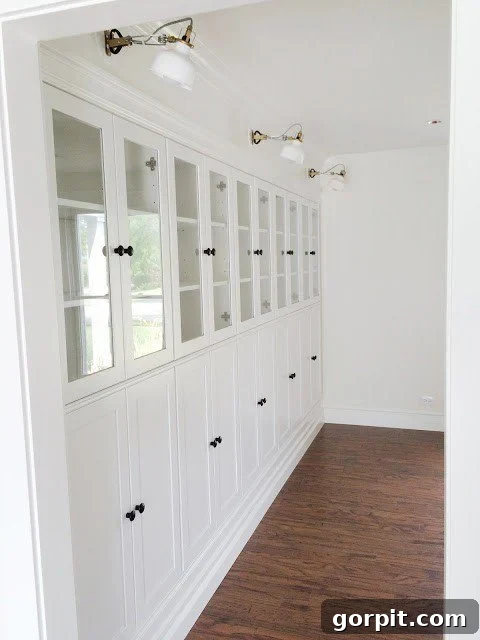 A row of white IKEA Borgsjo bookcases have glass doors on the top half and long cabinet doors on the bottom. This DIY IKEA hack provides gorgeous built-in shelves. 