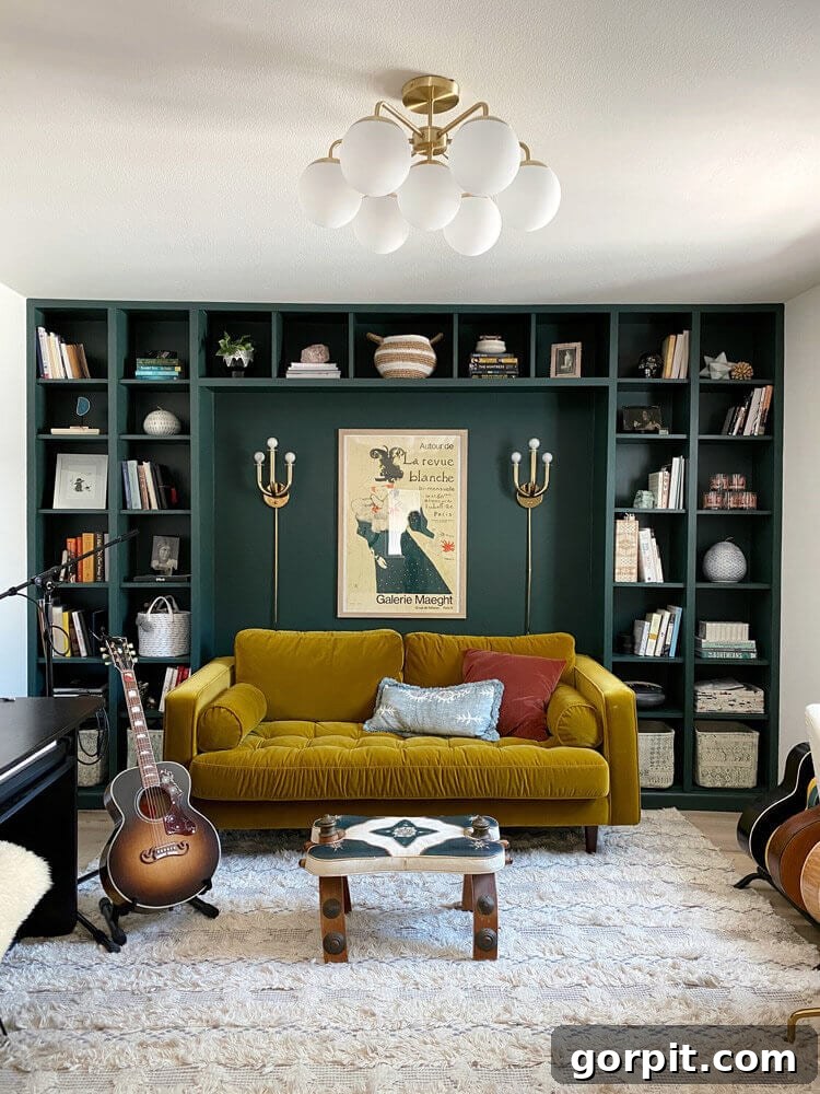 A music room with a dark green wall behind a yellow couch and many guitars. The wall has built-in shelves made from a DIY IKEA hack using Billy bookcases. 