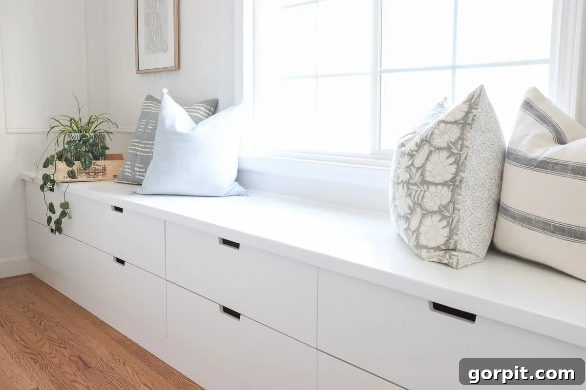 A white window seat made from IKEA Nordli drawers lines the living room wall under the window. The pillows and plant on the long bench have storage drawers below.