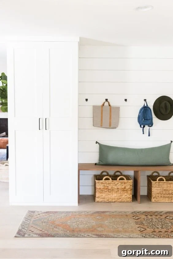 A mudroom setup along the outside wall of a house was made using DIY IKEA hacks like customizing a Pax high cabinet with drawers and a bench with storage underneath. Bags and hats are hung on hooks above the bare bench. 