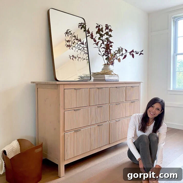 A smiling woman sits on a wooden floor next to a fluted Hemnes dresser altered using DIY IKEA hacks.