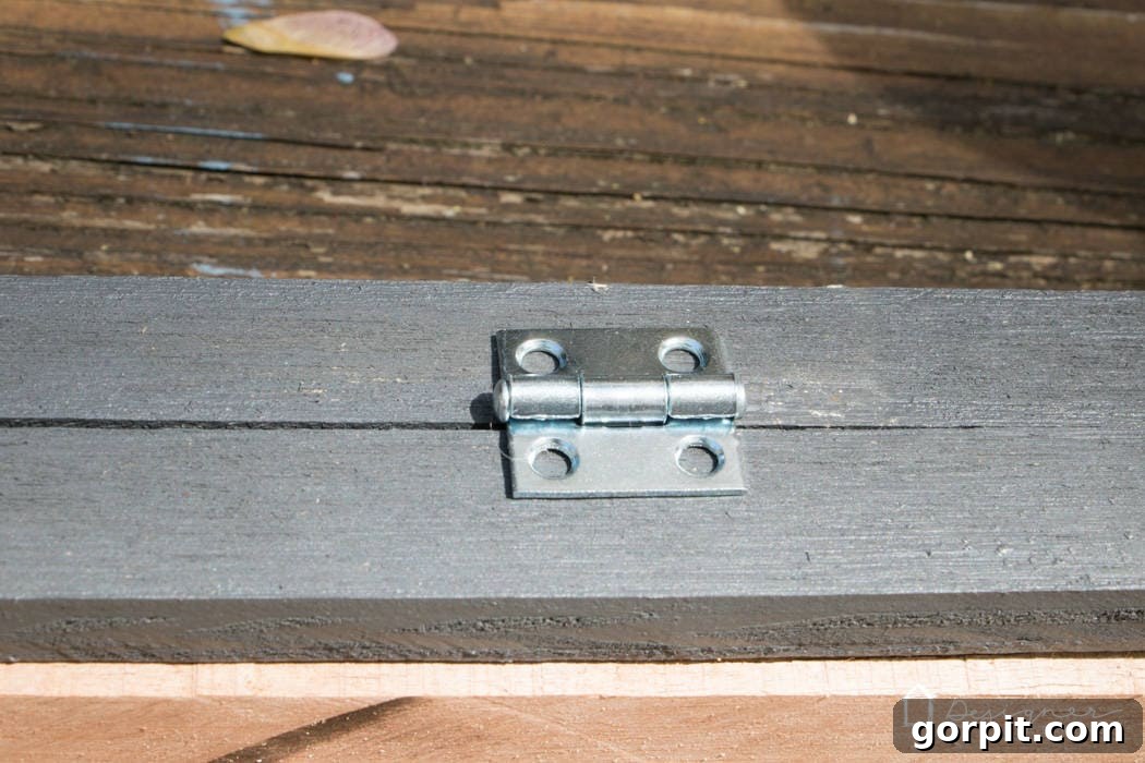 Detailed shot of a utility hinge being screwed into a reclaimed wood frame, showing the secure connection points for the hinged backer strip.
