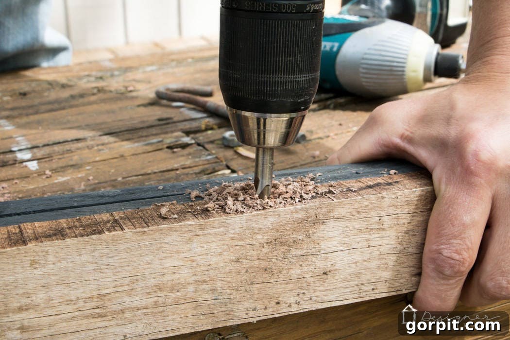 Drill creating a pilot hole in the top of a reclaimed wood frame for a screw hook, an integral part of the unique pipe hanging system.