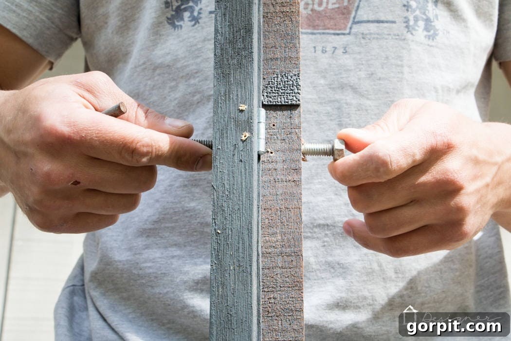 Screw hooks securely fastened with nuts into the top of a reclaimed wood frame, ensuring robust suspension from an industrial pipe.