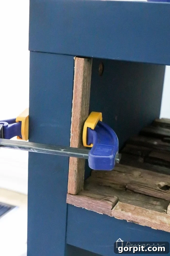 IKEA Lack Transformation: Designer Style for Less 10 A close-up shot of wood mosaic pieces being glued into the side of the IKEA Lack shelf, with a clamp holding the initial piece for proper curing.
