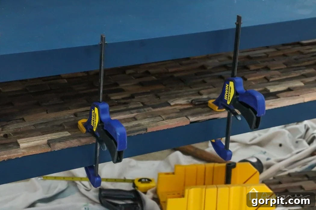 IKEA Lack Transformation: Designer Style for Less 11 The final step in the IKEA Lack hack, showing the bottom wood mosaic tiles being glued into place, with clamps securing the edges.