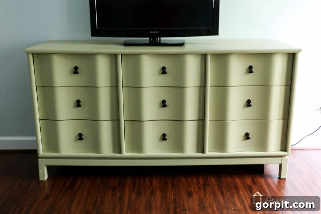 Wood Wonders: Your Guide to Transforming Furniture with Paint 2 A light green-yellow dresser with curved drawer fronts has a flat screen TV on it and is against a light blue wall on a hardwood floor.