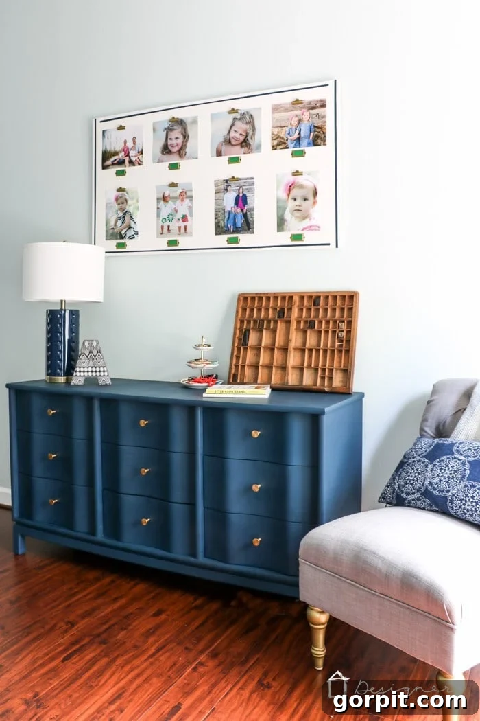 Wood Wonders: Your Guide to Transforming Furniture with Paint 12 Blue painted dresser with gold knobs next to a gray tufted armchair, topped with decor and books. A large photo collage of children is hanging on the wall above.