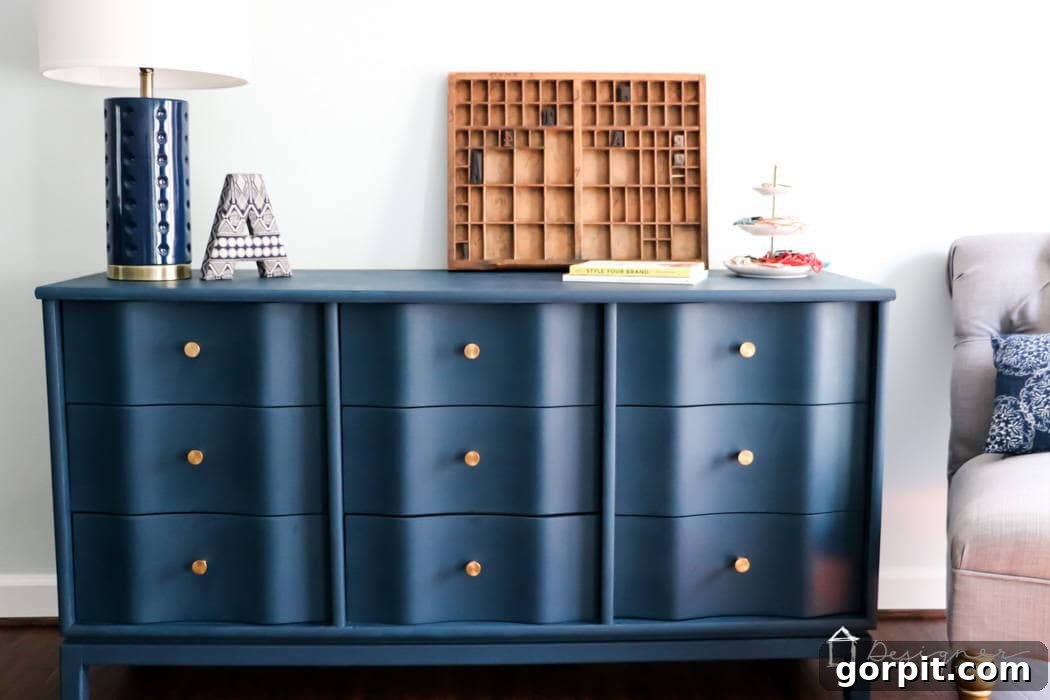 Wood Wonders: Your Guide to Transforming Furniture with Paint 8 Bold navy blue dresser with gold knobs and a wavy front has a and a smooth finish. Modern decor and a few books sit on top and a gray chair is to the right. A great example of a successful DIY makeover showing how to paint wood furniture for long-lasting results.