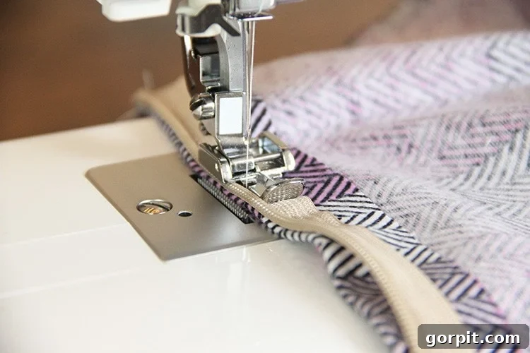 Sew Your Own Zippered Pillow Cover 12 A sewing machine finishes stitching the second side of a zipper to fabric, showing the zipper foot in action for a clean seam.