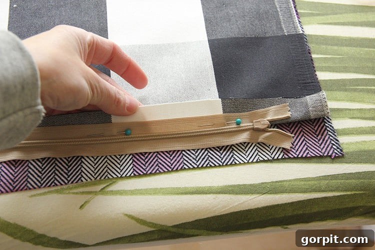 Sew Your Own Zippered Pillow Cover 6 A zipper is carefully pinned to the pressed edge of a fabric piece, demonstrating the correct alignment for sewing a zippered pillow cover.