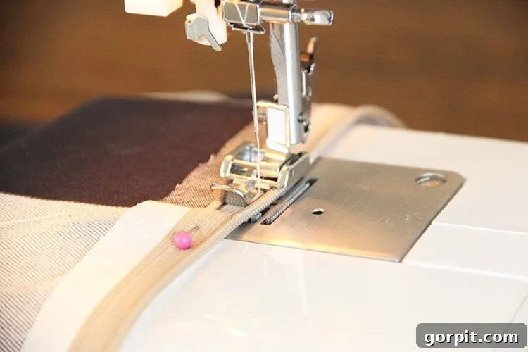 Sew Your Own Zippered Pillow Cover 9 A sewing machine needle stitches precisely along the edge of an open zipper, demonstrating how to attach the first side of the zipper to fabric.
