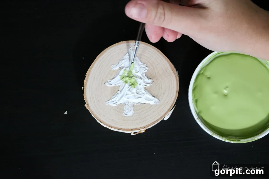 A textured Christmas tree caulk design on a wood slice, now painted in two shades of green, demonstrating the paintability of the caulk.