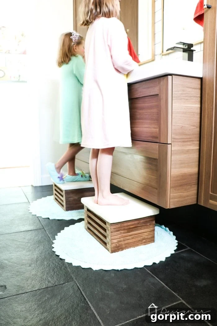 Beyaz Beton Yüzeyli Ahşap Basamak Taburesi Kendin Yap Projesi 10 View of two matching DIY wooden step stools neatly tucked under a floating bathroom vanity, illustrating their perfect fit.