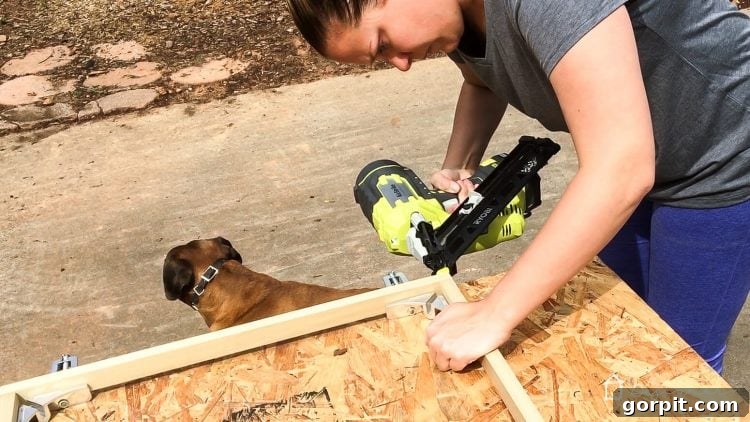 A nail gun securing two pieces of wood together, forming a sturdy corner of the DIY large wall art frame.