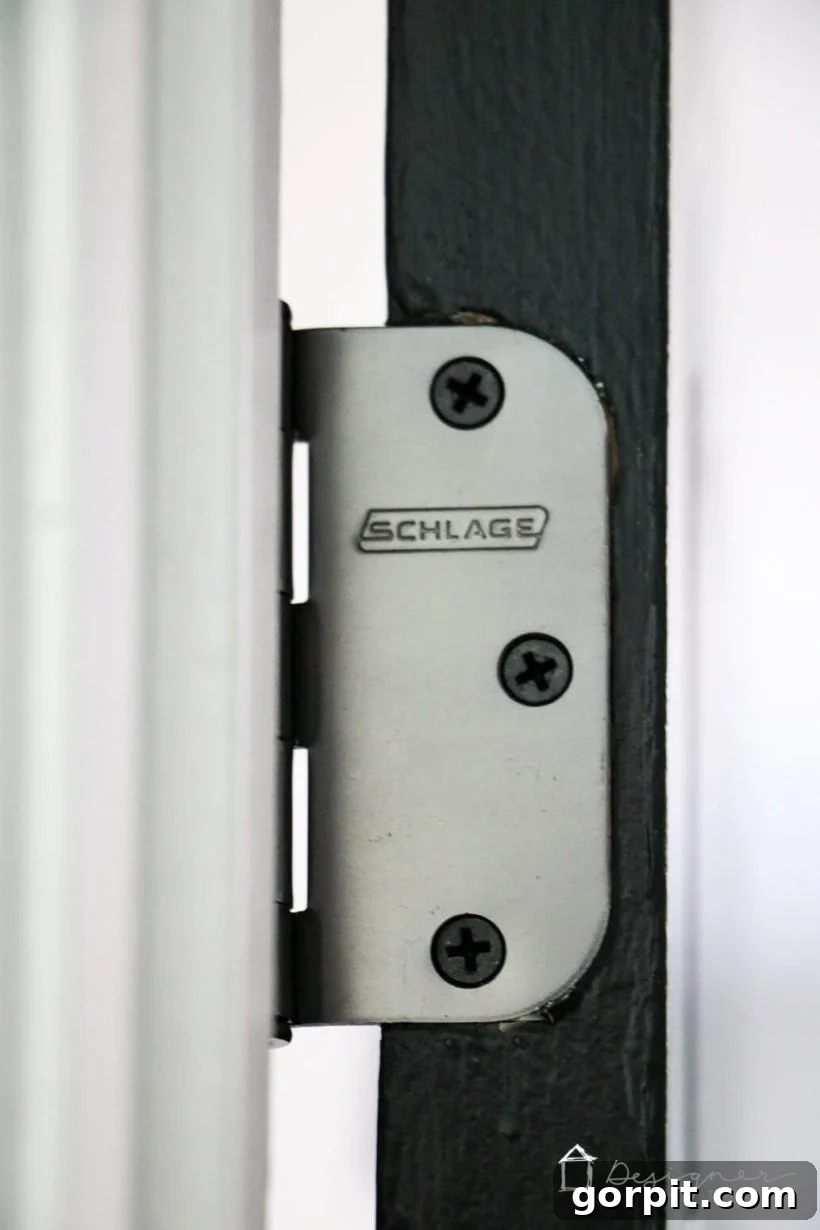 The Solution for Your Stubborn Door 4 Close-up of an oil-rubbed bronze hinge on a black interior door, highlighting where a longer screw can be used.
