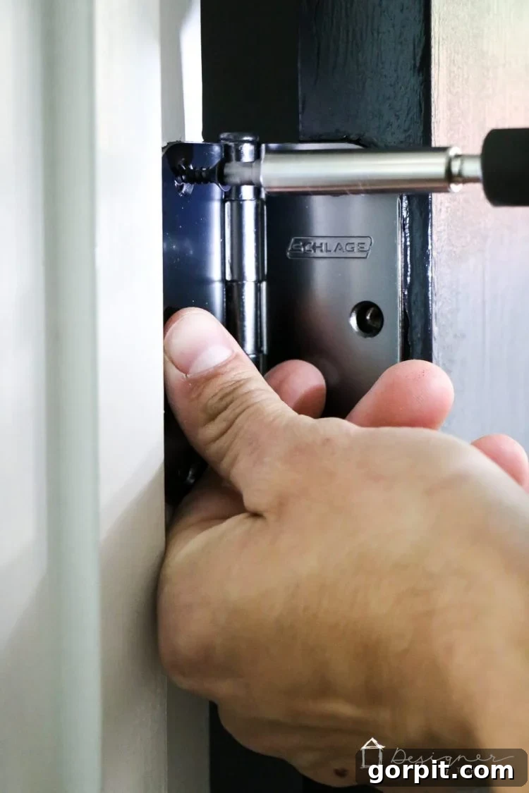 Installing new Schlage Aged Bronze hinges on a freshly painted black interior door.