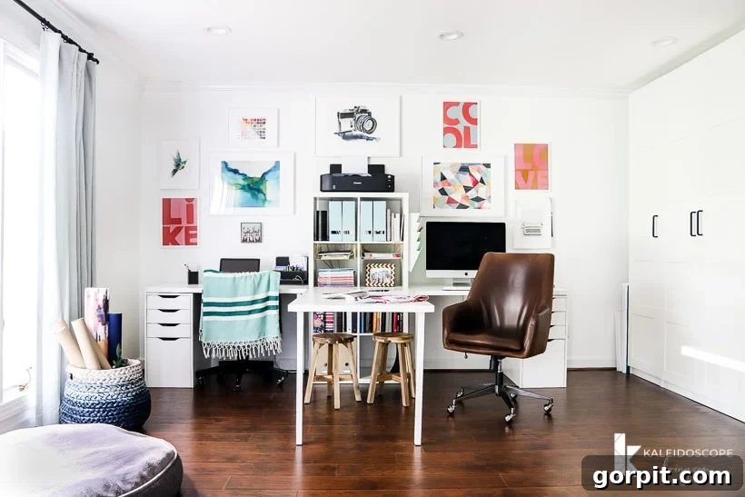 Smart IKEA Desk Upgrades for Less 11 A double desk has a table between two work stations, a leather wheeled chair, drawers, shelving units and a gallery wall on a dark wood floor. IKEA desk hacks can be used for office and crafting space. The words "Kaleidoscope Loving.com" are in the corner.