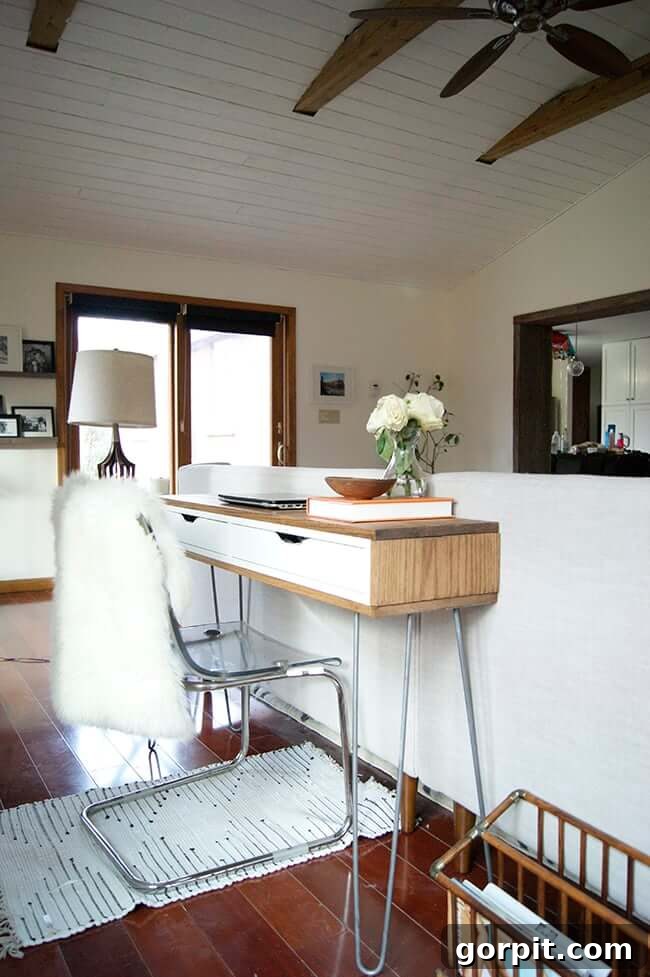 Smart IKEA Desk Upgrades for Less 9 A large living room with a slim IKEA desk behind the white couch. The high ceilings and fan highlight the minimalist room.