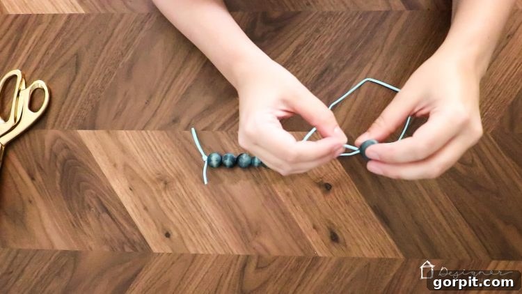 Detailed shot of stained wood beads being threaded onto a suede cord in a repeating pattern.