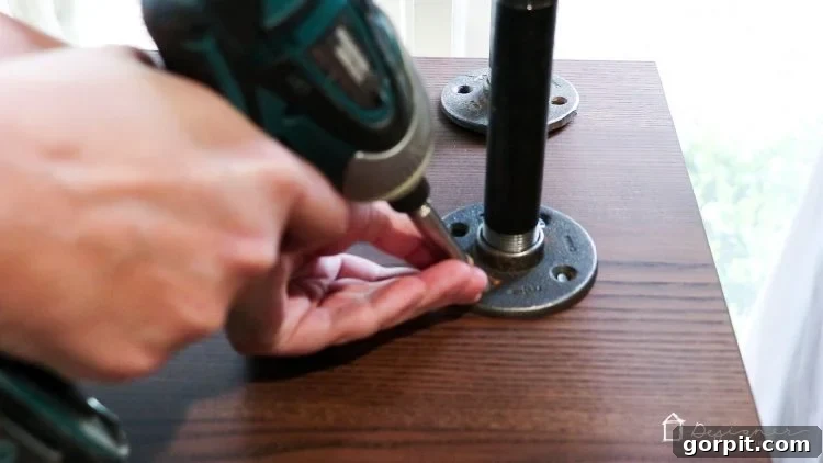 The assembled industrial top with pipes and flanges is carefully positioned and secured to the top surface of the Ikea Malm dresser.