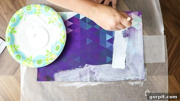 Applying a top coat of Mod Podge over the fabric-covered chipboard to seal and protect the surface.