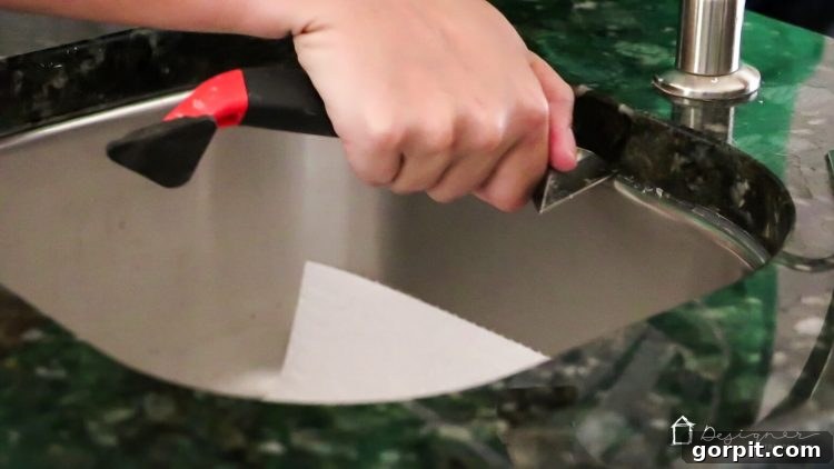 Seamless Caulk Replacement Guide 5 Using a caulk removal tool to scrape old, dirty caulk from a kitchen sink joint.
