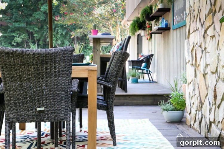A close-up of the outdoor dining table set with place settings, showcasing the quality of the Teak wood and the design of the wicker chairs on the beautifully stained deck.