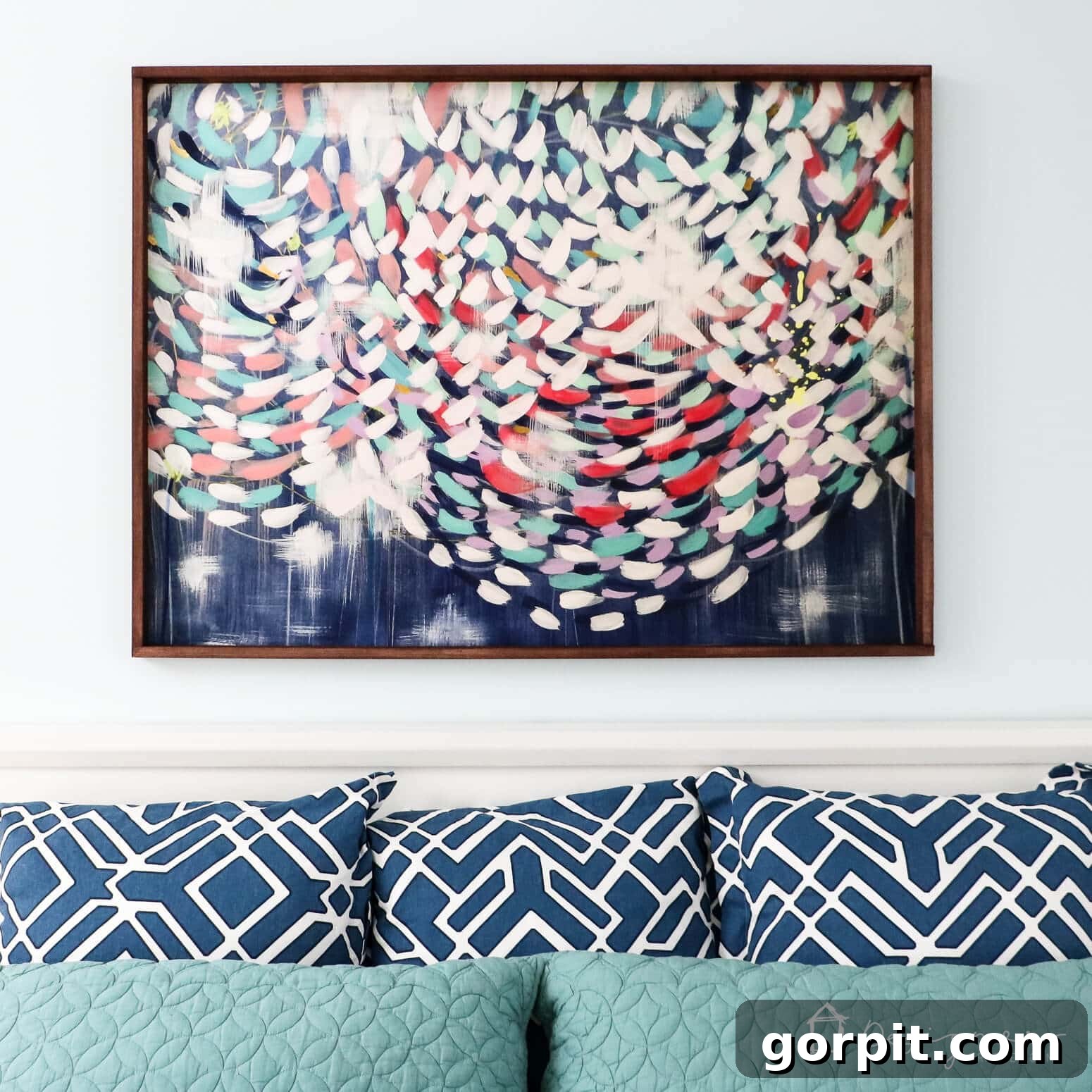 Crafting Stunning Frames for Your Big Art 10 You can learn how to make a picture frame like this thin dark wood frame holding a colorful art print above a teal bedboard with blue pillows.