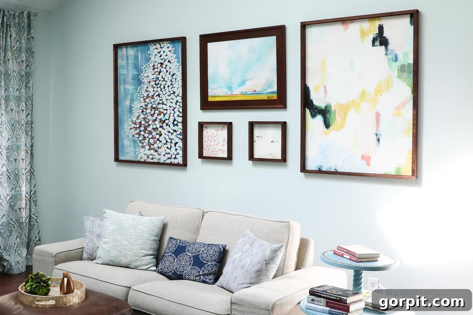 Crafting Stunning Frames for Your Big Art 15 A gallery wall comprised of six abstract art pieces of varying sizes, each framed in dark wood made by following the "How to Make a Picture Frame" tutorial, above a cream-colored couch with blue and white pillows.