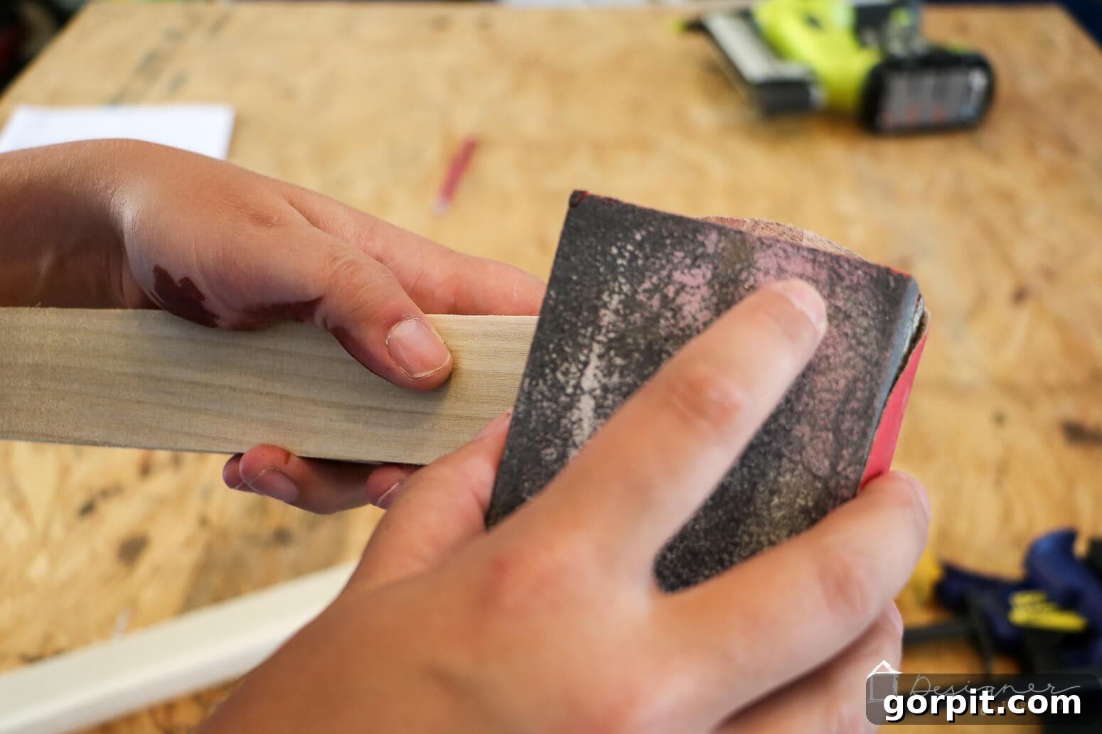 Crafting Stunning Frames for Your Big Art 5 Tasha's hand uses a block of sandpaper on a portion of a wooden frame, part of her instructional series on how to make a picture frame.