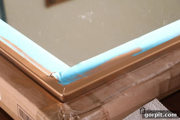 Using painter's tape to protect the mirror glass before applying Rub N Buff for a precise faux gold finish.