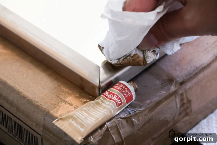 Applying Rub N Buff in Antique Gold to a metal mirror frame for a DIY faux gold finish.
