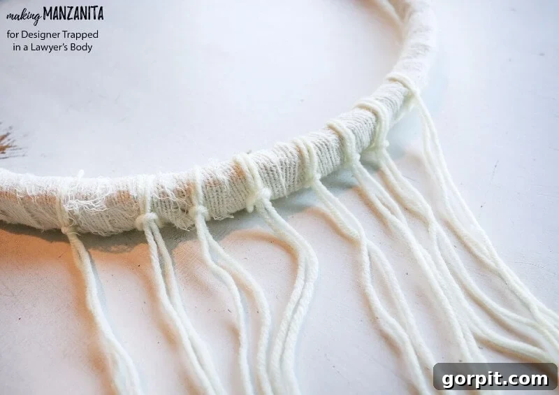 Close-up of yarn and fabric strips being attached to an embroidery hoop for a boho winter wreath
