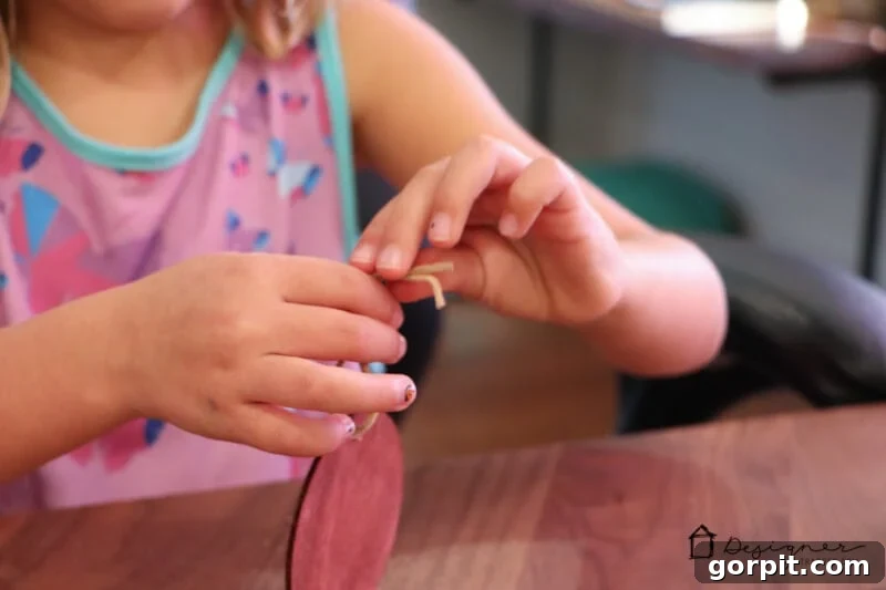 Children's hands threading suede cord through a DIY photo Christmas ornament, adding a hanger.