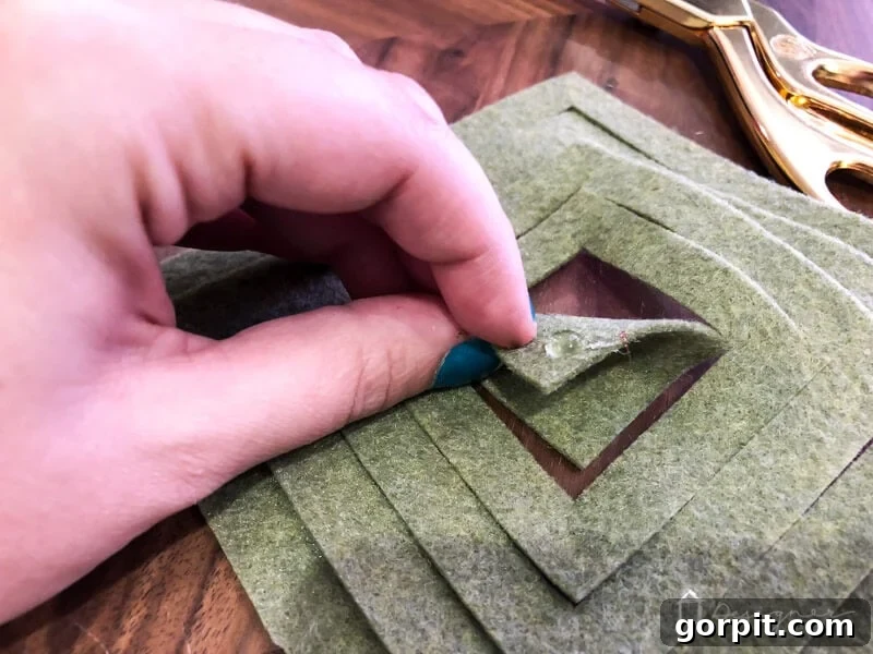 Warm & Fuzzy Holidays: Crafting One-of-a-Kind Felt Ornaments 6 Step-by-step guide: folding and hot gluing the first corner of a DIY felt Christmas ornament to create a stunning 3D effect for your holiday decor.
