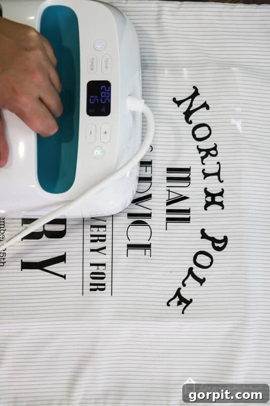 Close-up photo of using a Cricut EasyPress to iron heat transfer vinyl onto a DIY Santa sack