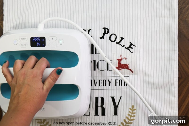 Applying heat transfer vinyl for a child's name onto a DIY Santa sack, demonstrating the personalization step