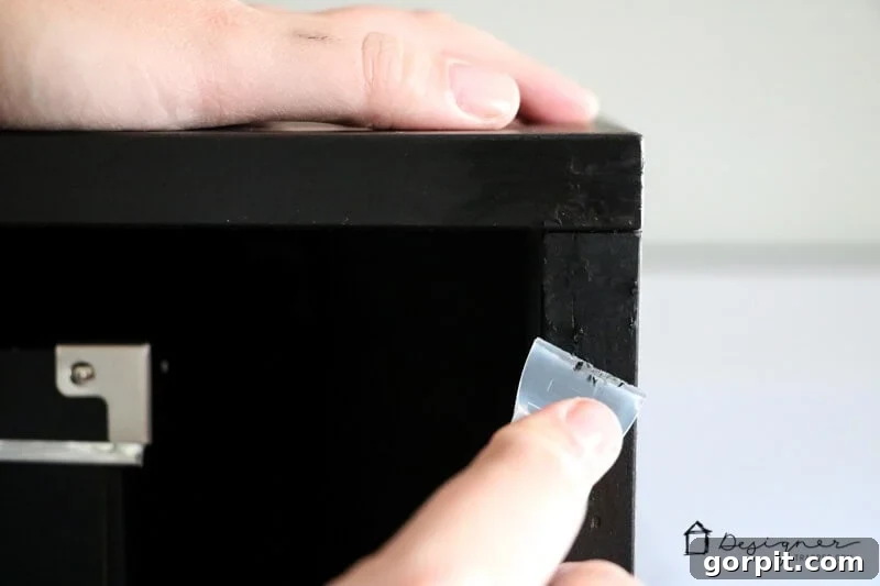 A woman's hand uses a Leveler Cap to carefully scrape off any excess residue from a repaired piece of furniture, ensuring a smooth and clean finish.