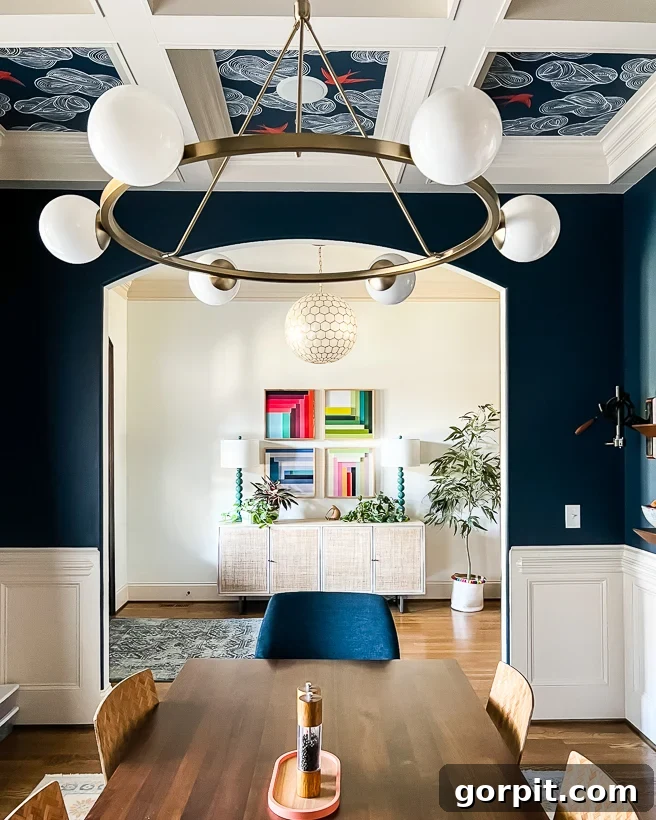 Make Small Rooms Feel Bigger 9 Genius Hacks 11 A dining room with deep blue walls, white shiplap, and a dining table. An arch into the hallways shows artwork and a credenza.