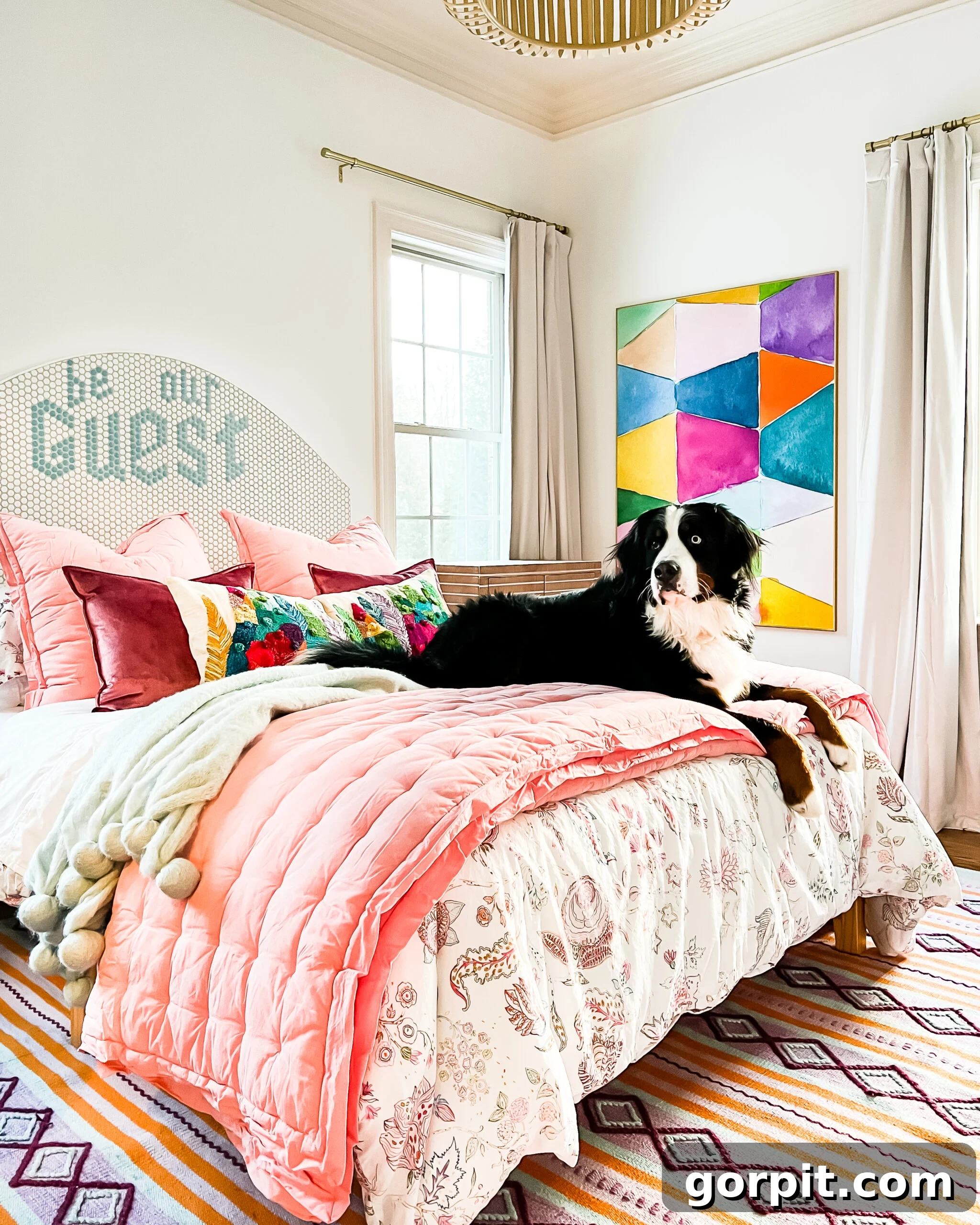 Make Small Rooms Feel Bigger 9 Genius Hacks 8 A dog on a bed with exposed legs and a headboard that reads, "be our guest." Colorful abstract art hangs on the wall.