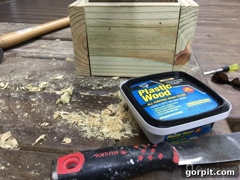 Applying wood filler with a putty knife into a screw hole on a raw wood surface. Demonstrates proper application technique.