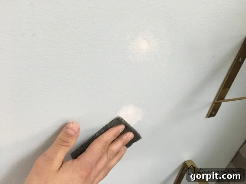 Sanding the dried spackle smooth after a drywall repair.