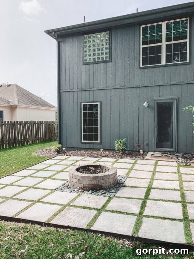 This fire pit idea uses pavers with astroturf in between and fire pit in middle, behind the house, creating a modern and integrated outdoor entertainment area.