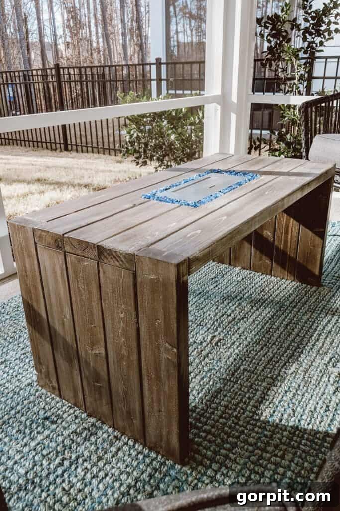 A back porch with a green outdoor rug and a simple planked coffee table with a built-in miniature fire pit, offering both warmth and surface space.